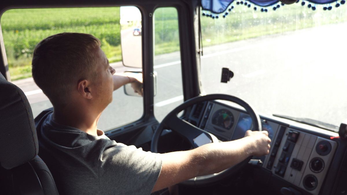 Man holds hand on the steering wheel and driving truck through countryside on a warm summer day. Profile of truck driver. Trucker inside at car. Side view Close up Slow motion.
